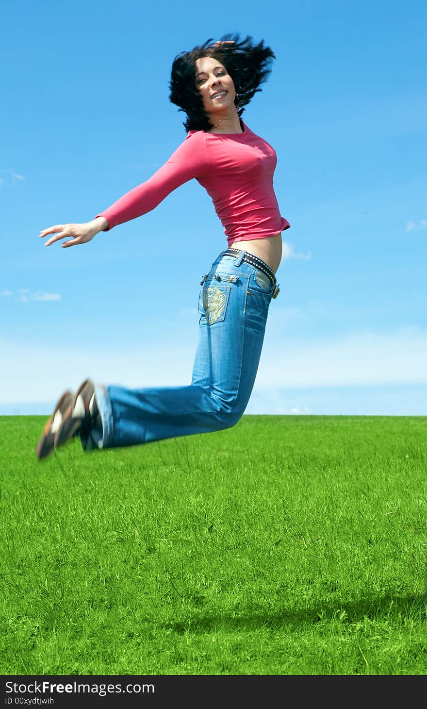 Woman jump in green field under blue sky