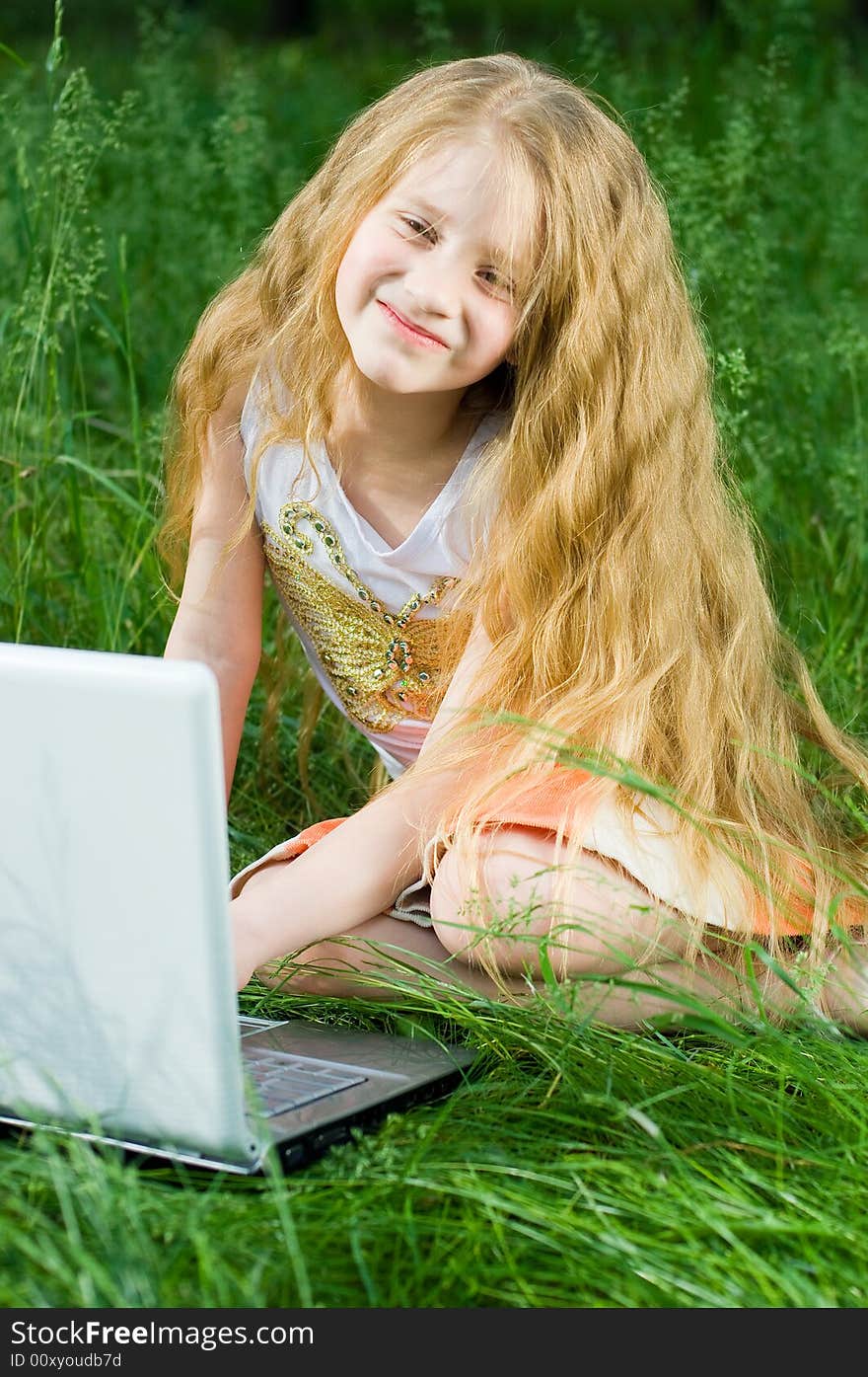 Funny little girl sitting with laptop in green grass. Funny little girl sitting with laptop in green grass