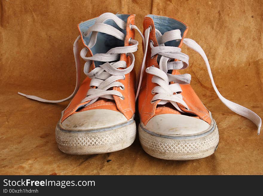 Pair of used orange sneakers on brown background