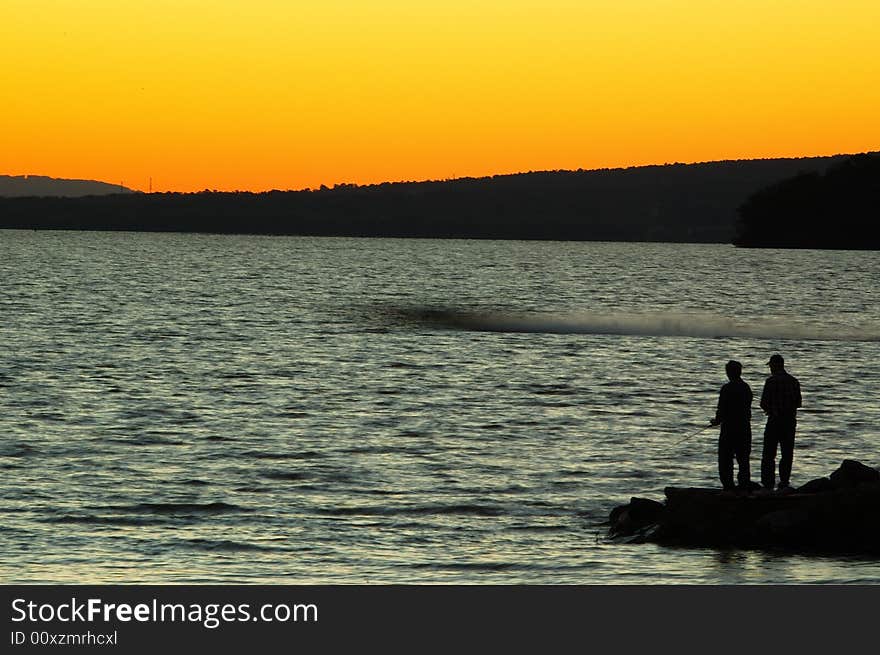 Sunset on a Lake With Fishermen on Shore a Boat Speeding on the Water. Sunset on a Lake With Fishermen on Shore a Boat Speeding on the Water