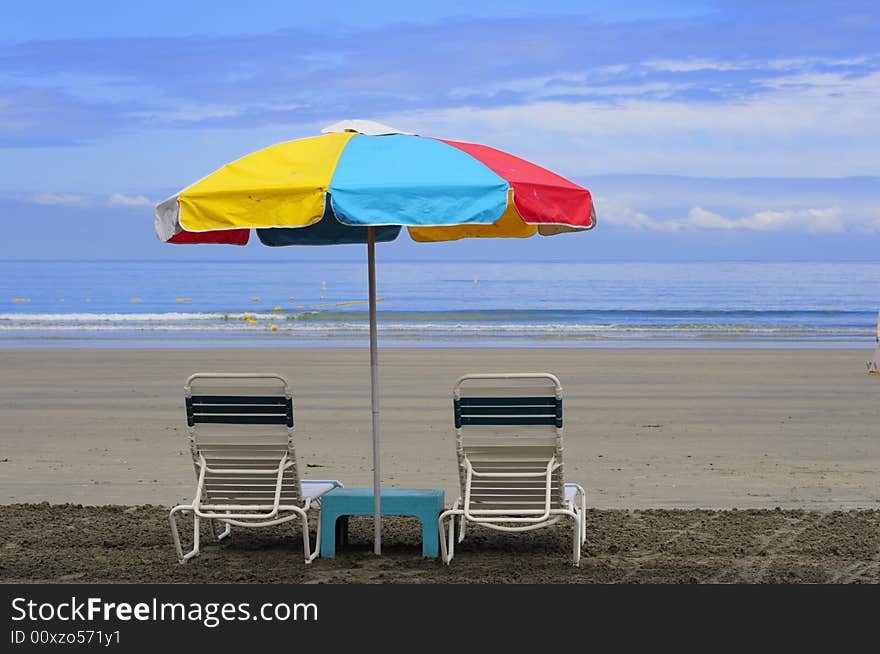 Two beach chairs under a colorful umbrella