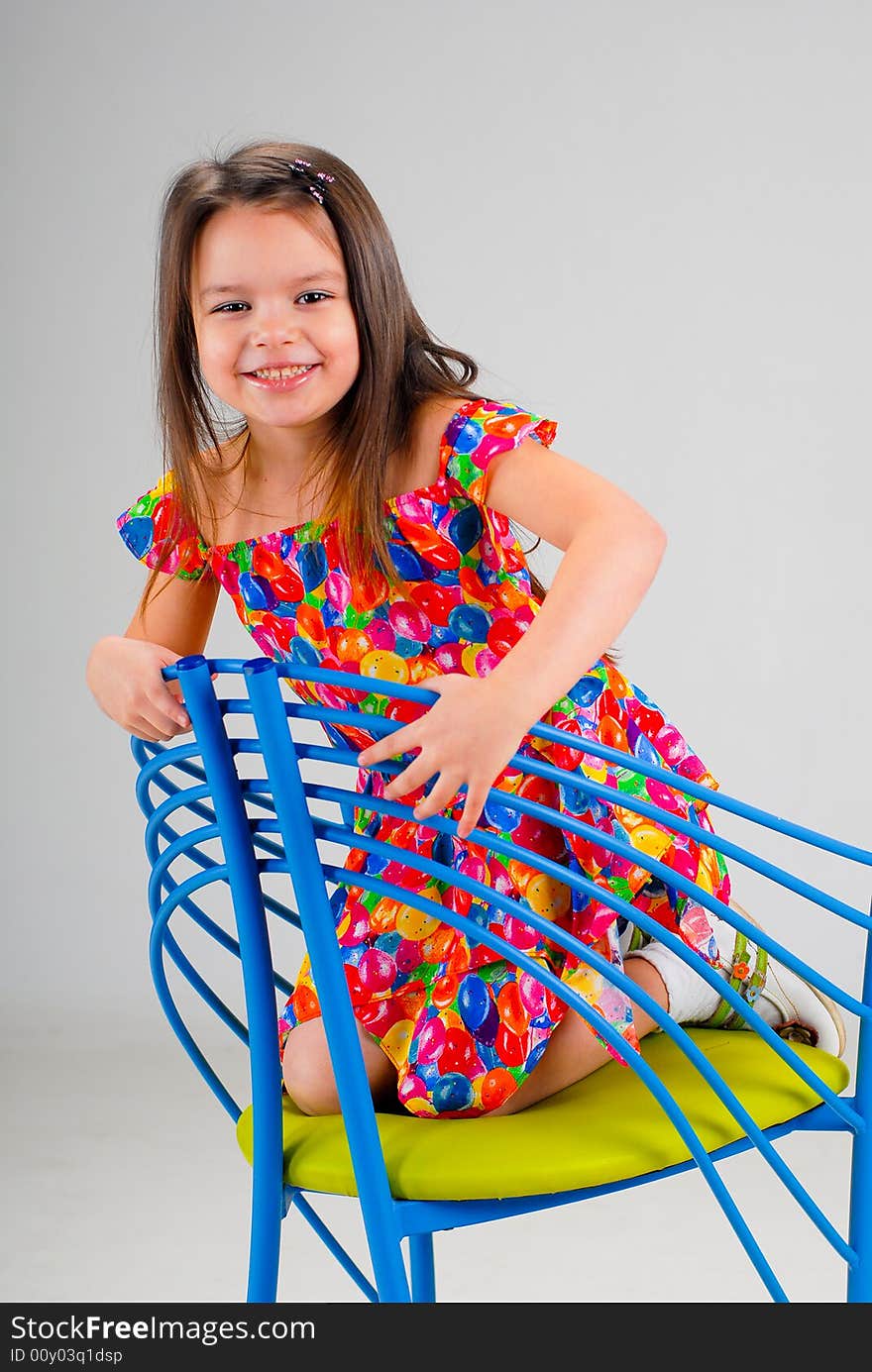 Little cute laughing brown-haired girl in red dress sitting on a chair. Little cute laughing brown-haired girl in red dress sitting on a chair