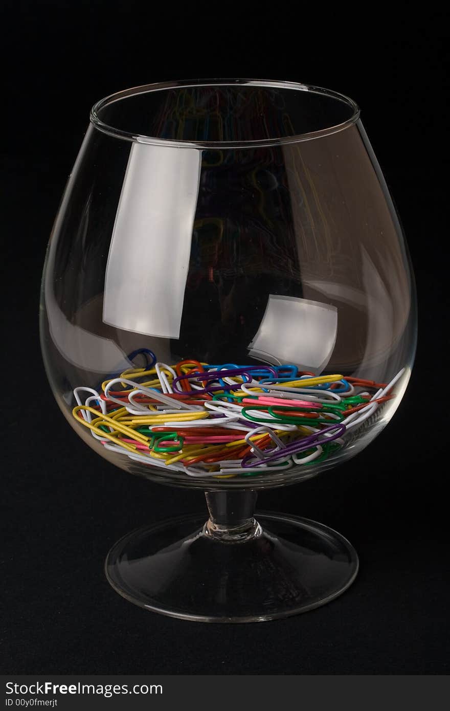 Colored paperclips in a glass on a black background. Close up. Selective focus.