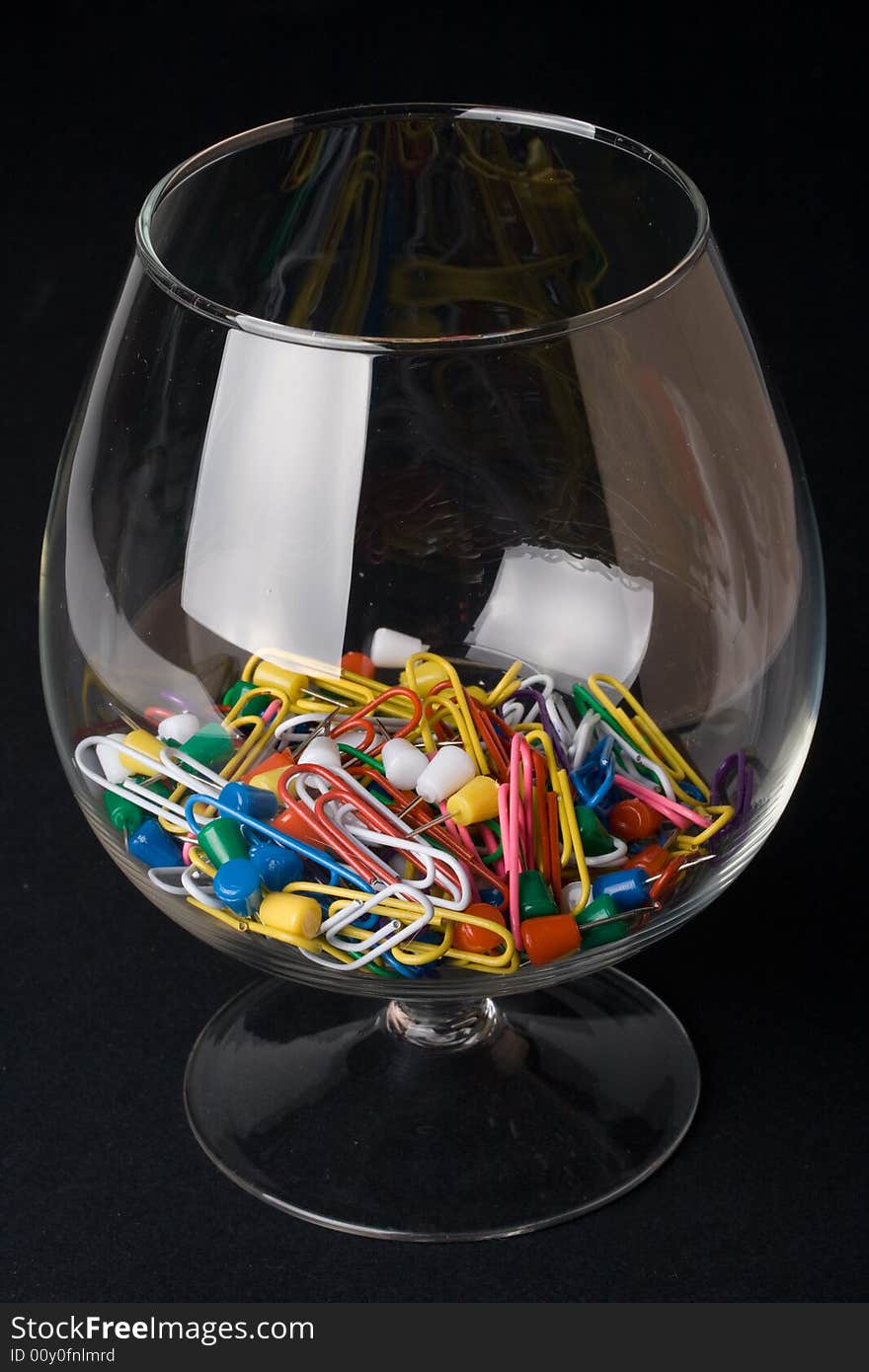 Colored paperclips and pins in a glass on a black background. Close up. Selective focus.