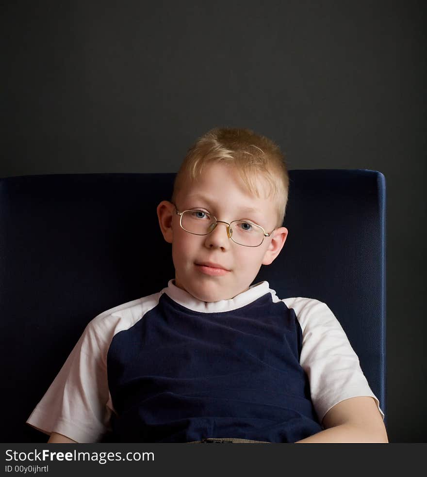 Confident boy sit on chair and look at camera. Over grey background.