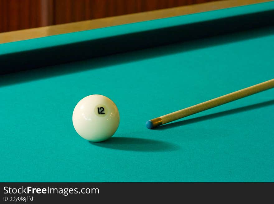 The white billiard-ball number 12 and wood cue on a green table. The white billiard-ball number 12 and wood cue on a green table