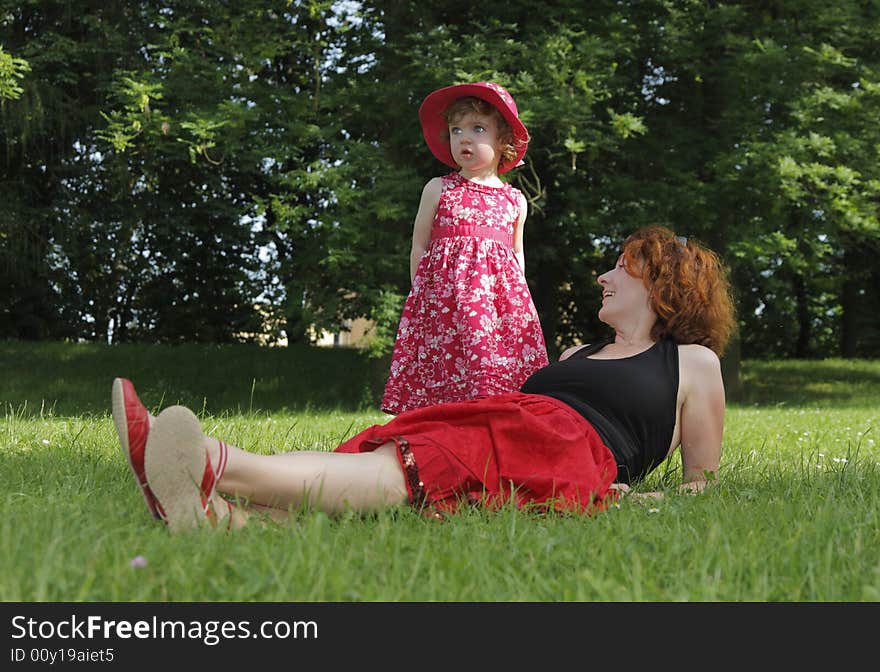 A happy woman is lying on the grass. Her daughter is standing near.