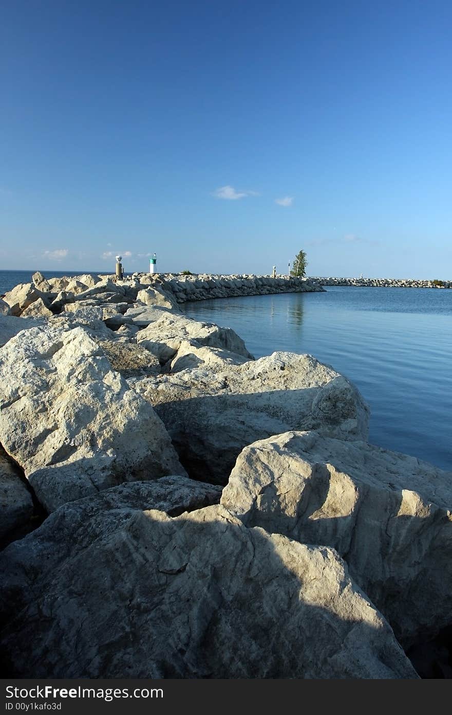 Trail of large boulders and lighthouse. Beautiful lake and clear sky. Trail of large boulders and lighthouse. Beautiful lake and clear sky.