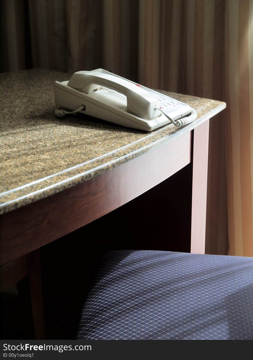 A white business phone on a desk, with a chair and lateral light.