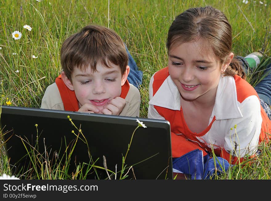 A pigeon pair lie on a green grass among the field colors and look in the screen of notebook. A pigeon pair lie on a green grass among the field colors and look in the screen of notebook