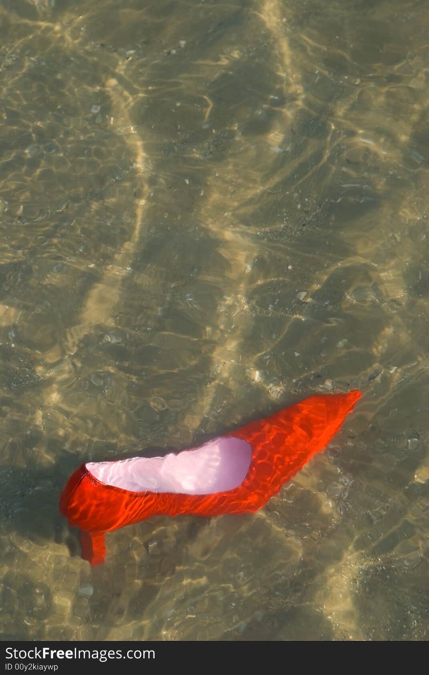 A red and pink stiletto shoe in shallow water. A red and pink stiletto shoe in shallow water