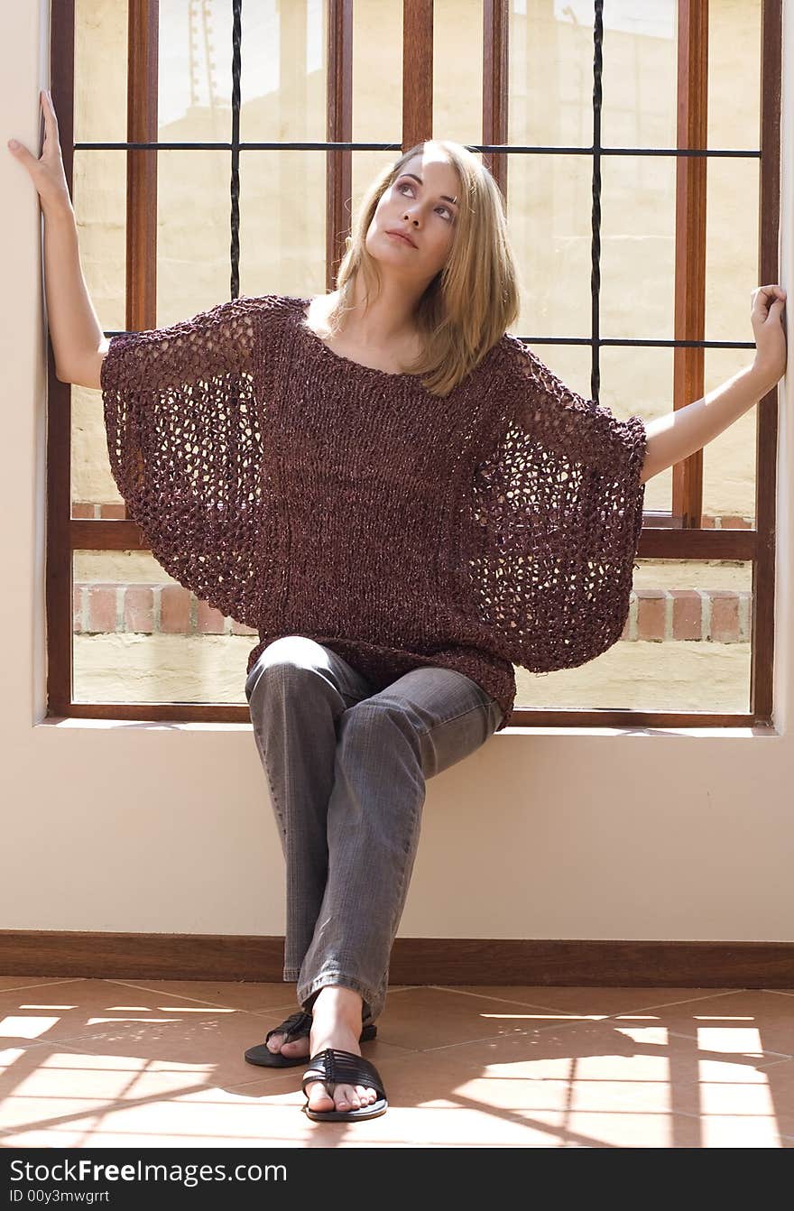 Blond girl sitting in the sun in windowsill thinking about the future. Blond girl sitting in the sun in windowsill thinking about the future