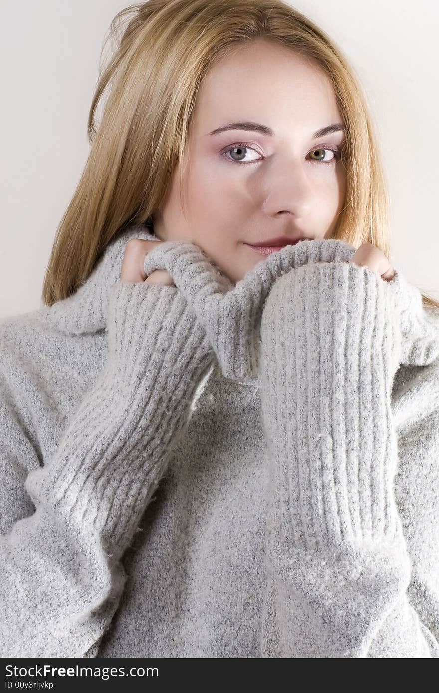 Beautiful blond girl in grey jersey hiding behind the neck and looking at the camera