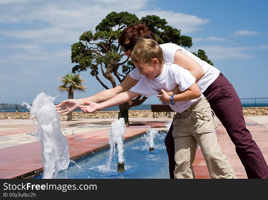 Mother and the son play and have fun at a fountain