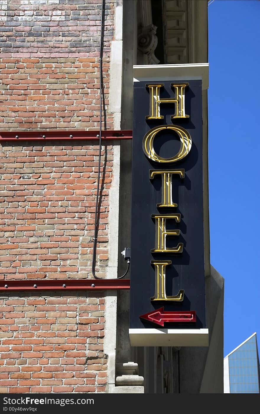 A neon sign for a hotel sign sticks out of a corner building.