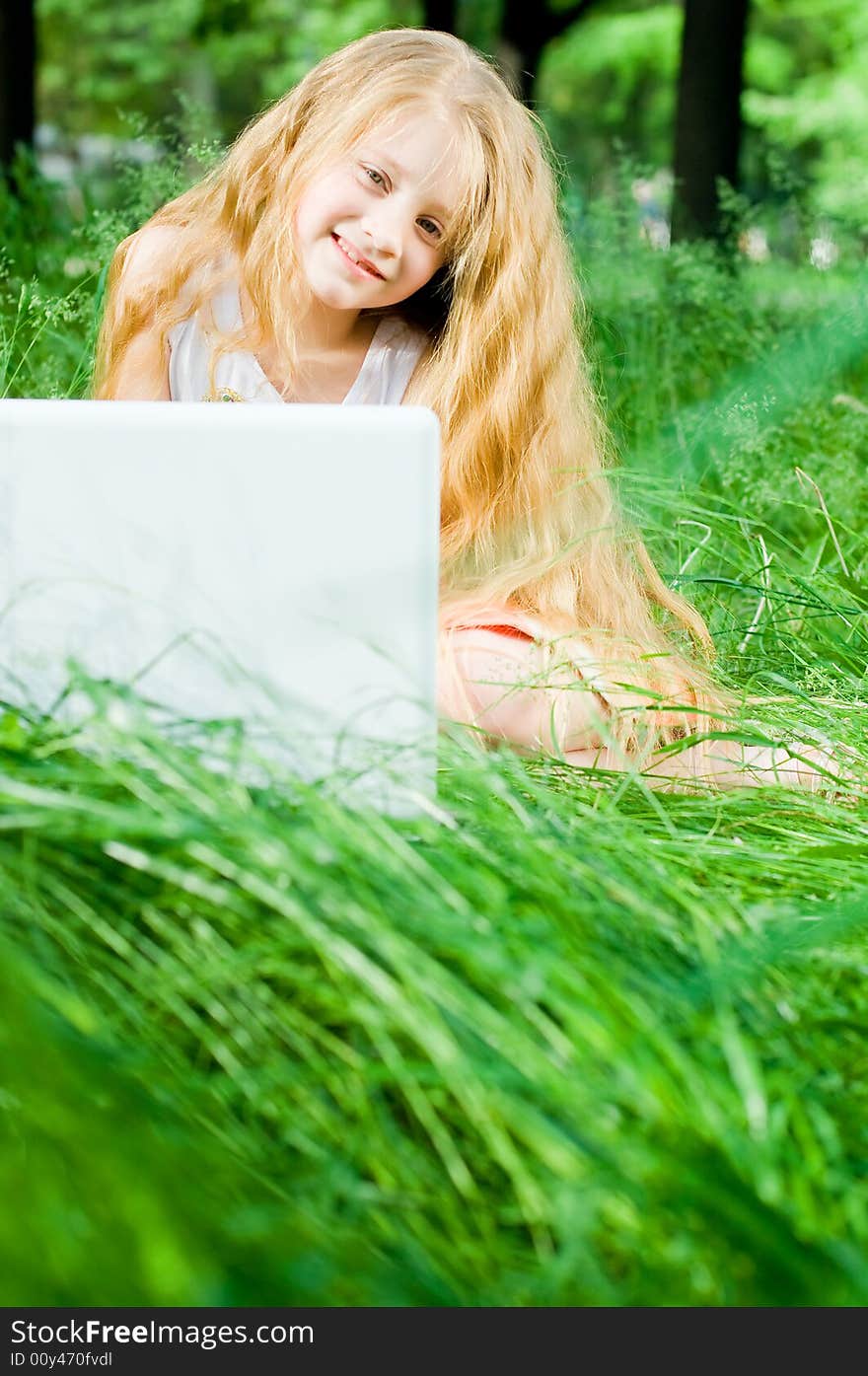 Smiling little girl with laptop in green grass