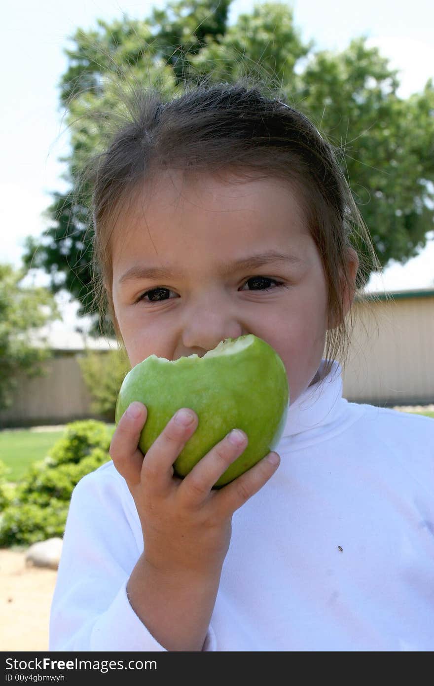 A young school age girl eats a green apple for a healthy snack. A young school age girl eats a green apple for a healthy snack