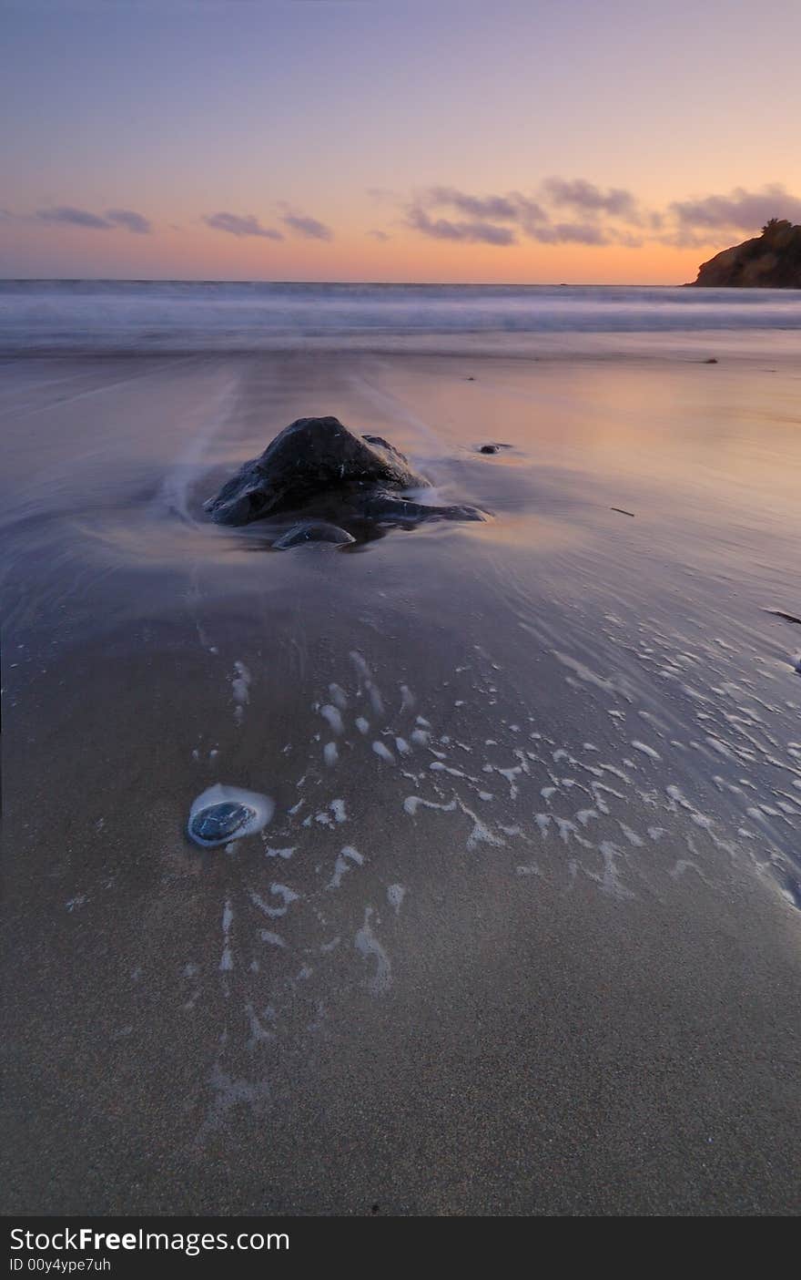 A rock on the shoreline at sunset