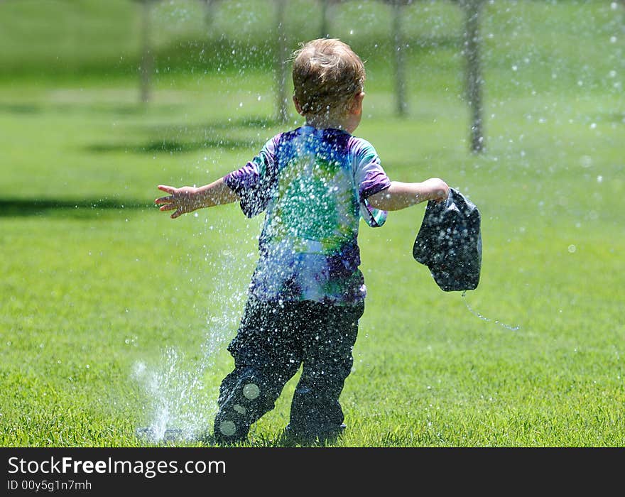 Young boy running away from water sprinkler trying not to get wet. Young boy running away from water sprinkler trying not to get wet