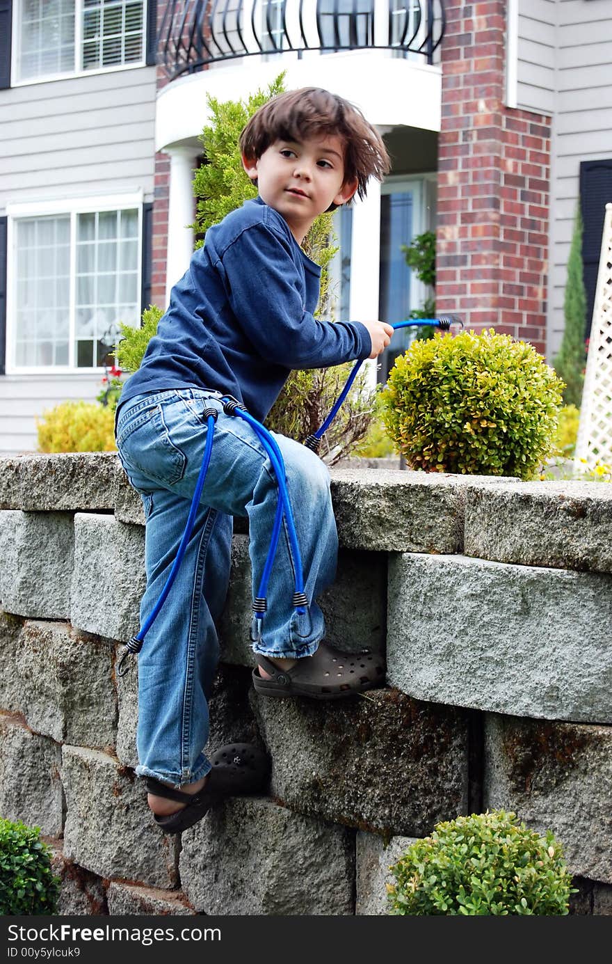 Adorable little boy top roping and climbing a stone garden wall using bungee cords as climbing rope. Vertically framed shot. Adorable little boy top roping and climbing a stone garden wall using bungee cords as climbing rope. Vertically framed shot.