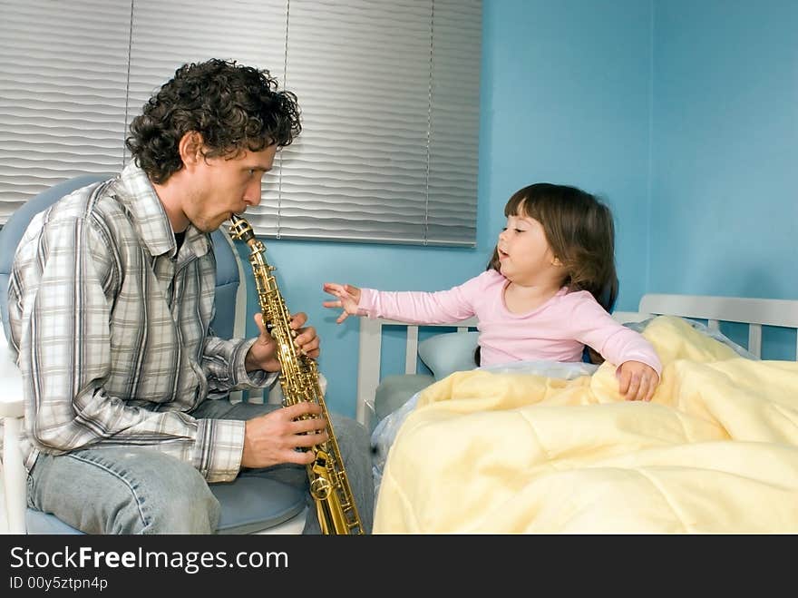 A father playing soprano saxophone for his daughter sitting in bed. A father playing soprano saxophone for his daughter sitting in bed.