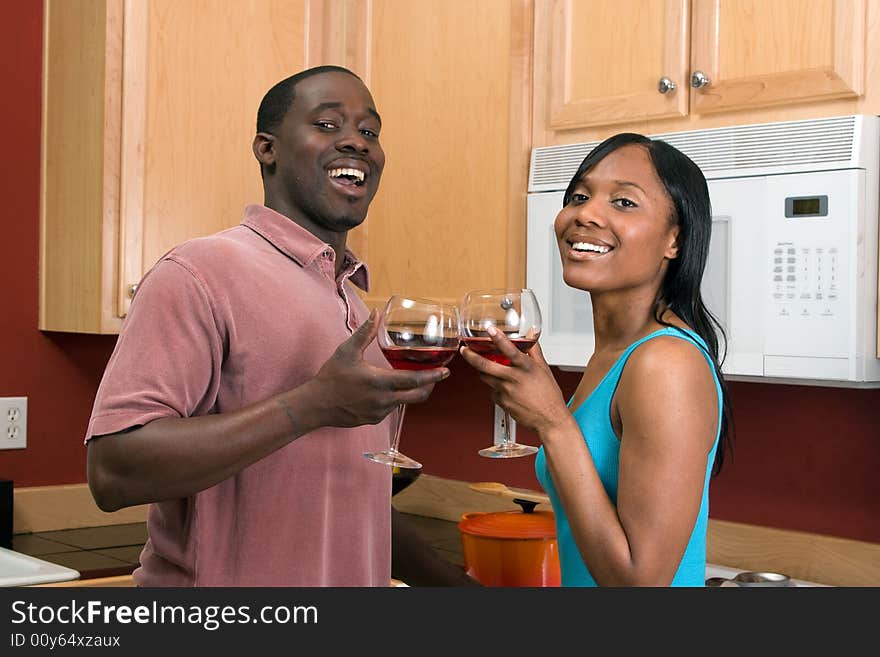 Attractive laughing young African American couple standing in a kitchen clinking wine glasses, in a toast. Horizontally framed, close cropped, shot with the man and woman looking at the camera. Attractive laughing young African American couple standing in a kitchen clinking wine glasses, in a toast. Horizontally framed, close cropped, shot with the man and woman looking at the camera.