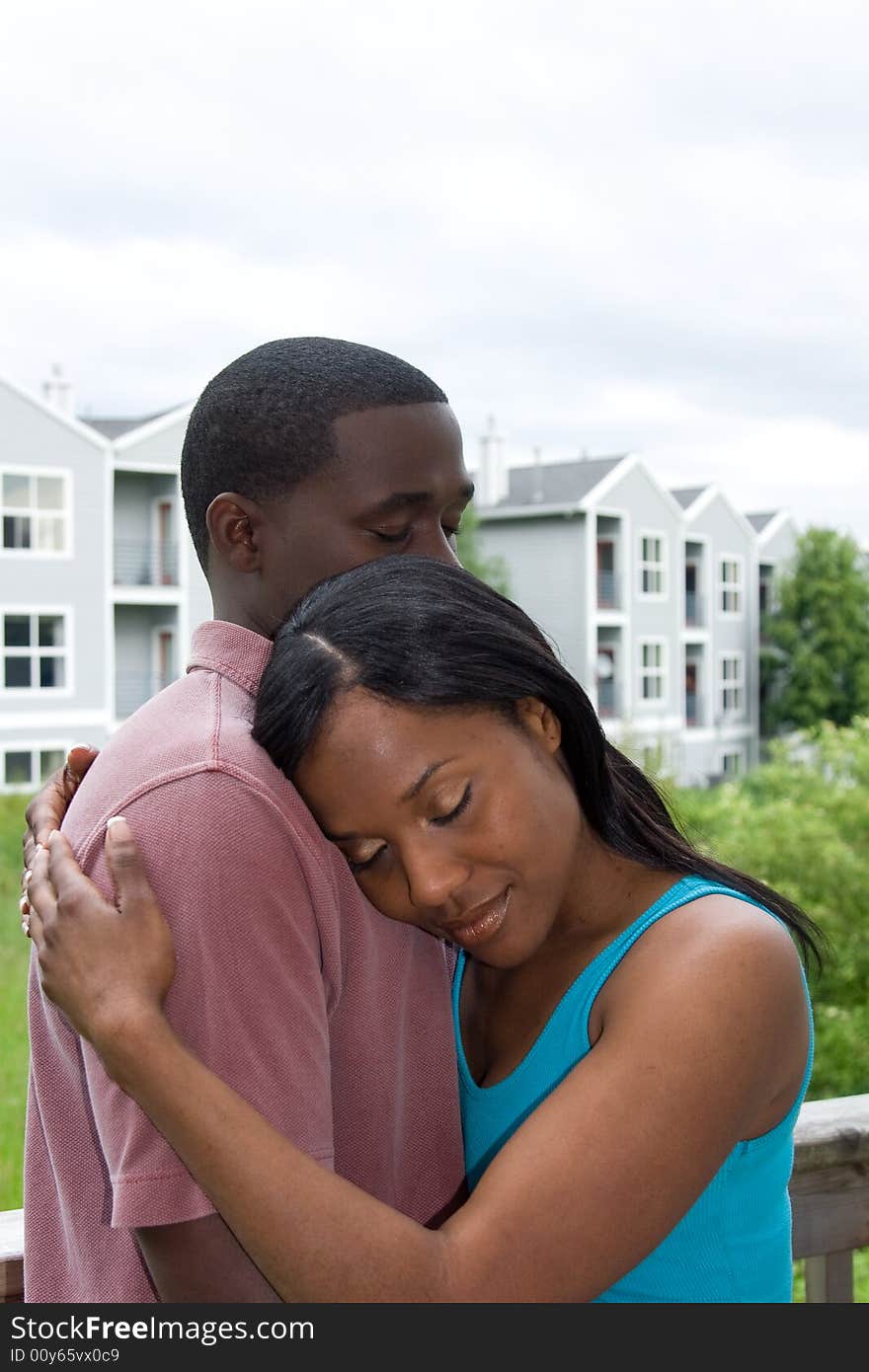 Attractive young couple in a embrace, with the womans head resting on the mans shoulder. Vertically framed outdoor shot on a deck. Attractive young couple in a embrace, with the womans head resting on the mans shoulder. Vertically framed outdoor shot on a deck.