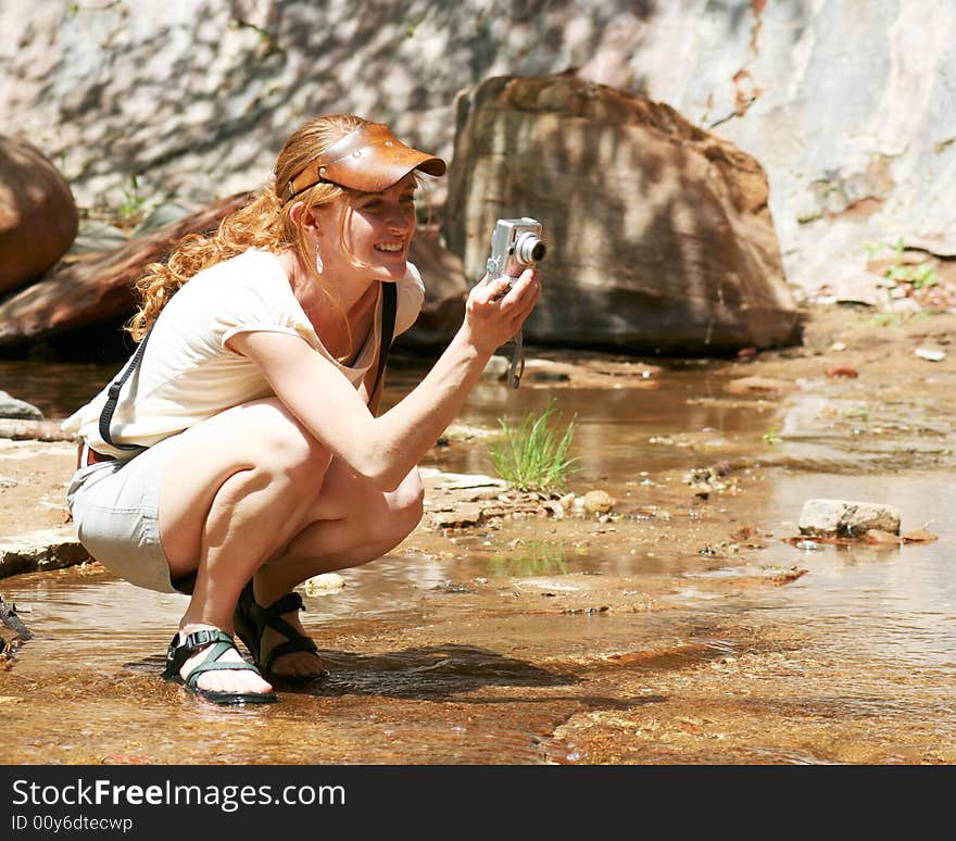 A beautiful young redhaired woman in a leather visor enjoys using her digital camera on a sunny day at the creek. A beautiful young redhaired woman in a leather visor enjoys using her digital camera on a sunny day at the creek.