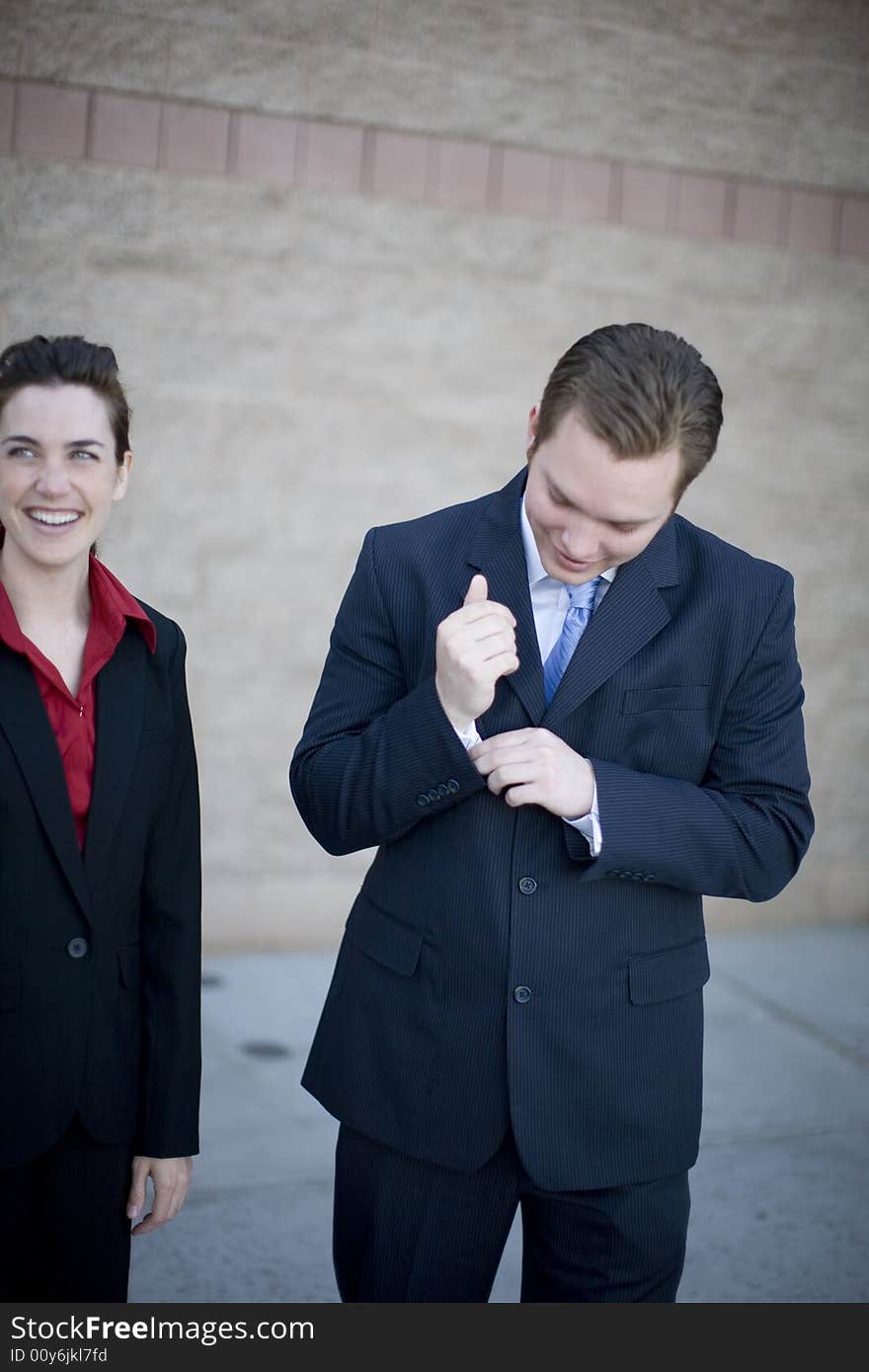 Businessman and businesswoman stand together smiling while man fixes shirt. Businessman and businesswoman stand together smiling while man fixes shirt