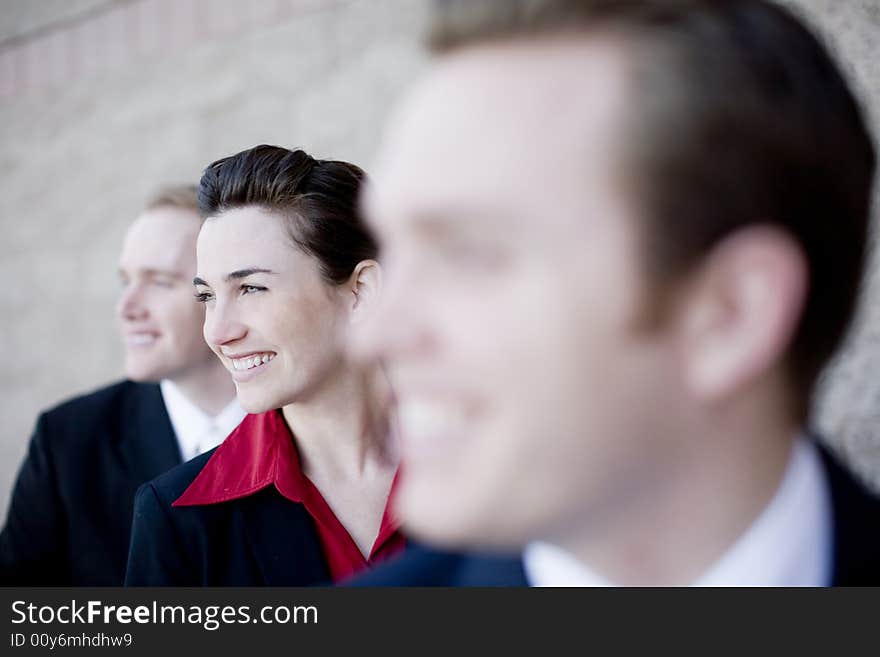 Three businesspeople standing in a line with young attractive woman in the middle smiling. Three businesspeople standing in a line with young attractive woman in the middle smiling