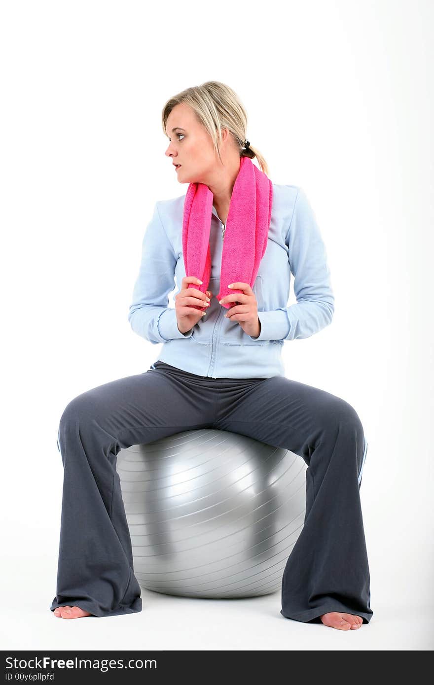 Blond woman in gym outfit exercising with a pilates ball holding a pink towel isolated on white