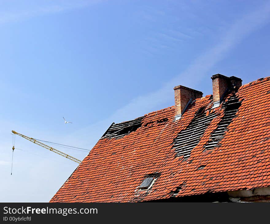 Deavastated roof closeup with yellow crane and bird in background. Huge holes in the red roof after fire.