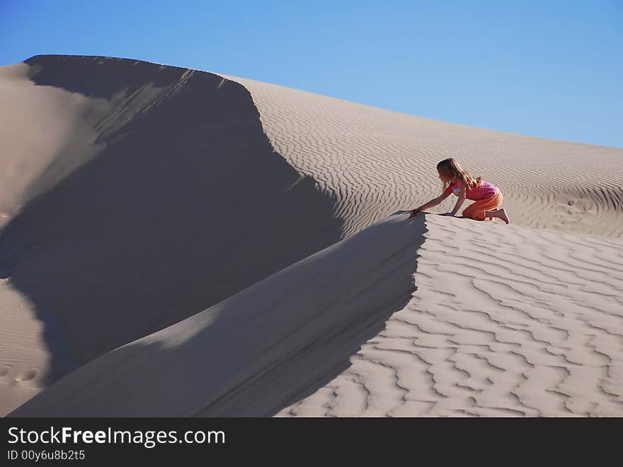 Horizontal shot of a young, six year old, girl wandering on a desolate sand dune in the deep desert. Horizontal shot of a young, six year old, girl wandering on a desolate sand dune in the deep desert