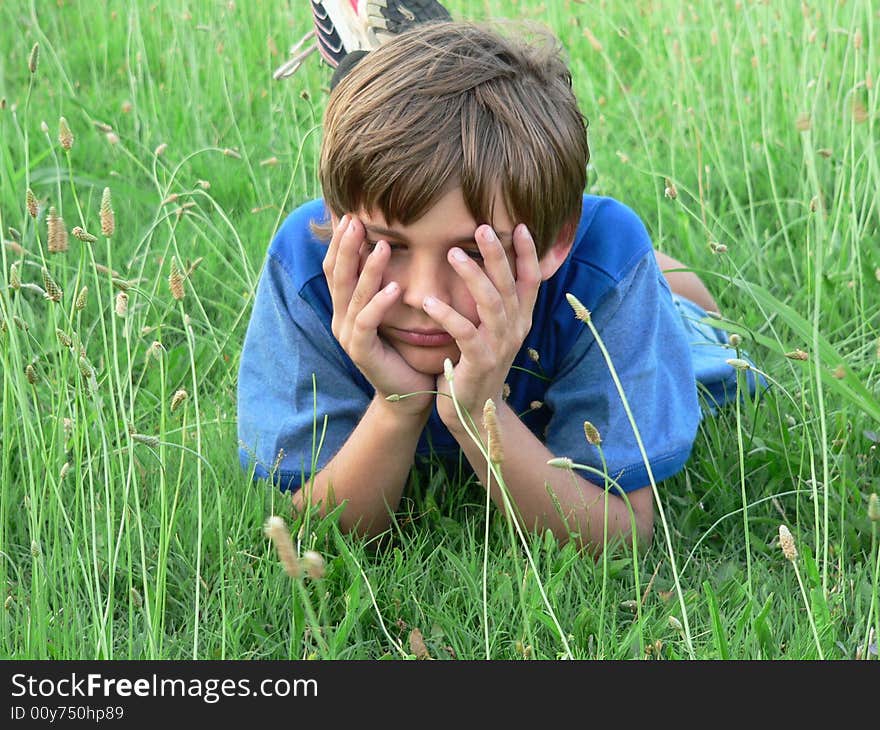 Boy in blue t-shirt with hands over eyes; he is lying in the grass/field. Boy in blue t-shirt with hands over eyes; he is lying in the grass/field