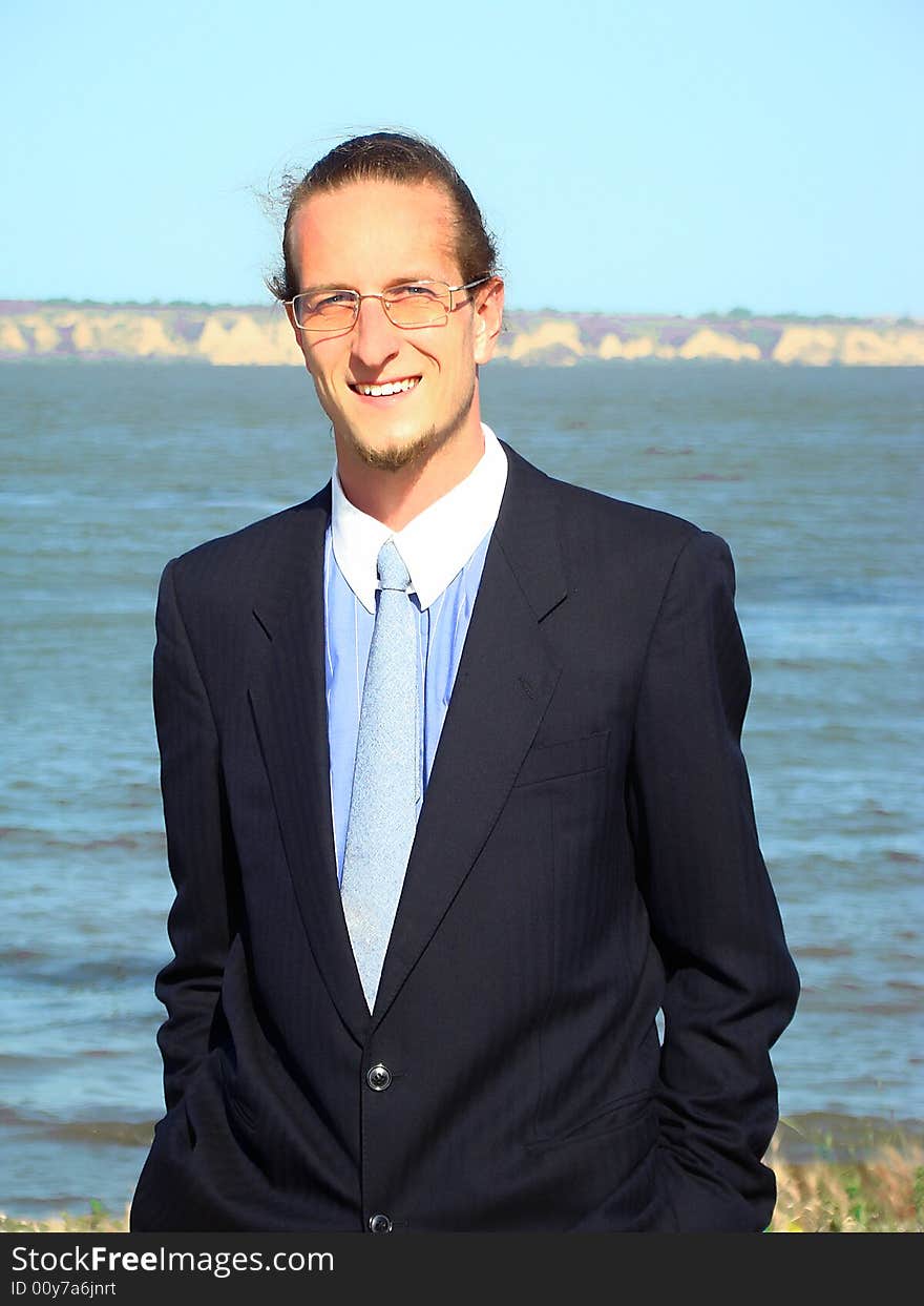 Young smiling business man with glasses and little beard on the riverside. Young smiling business man with glasses and little beard on the riverside.