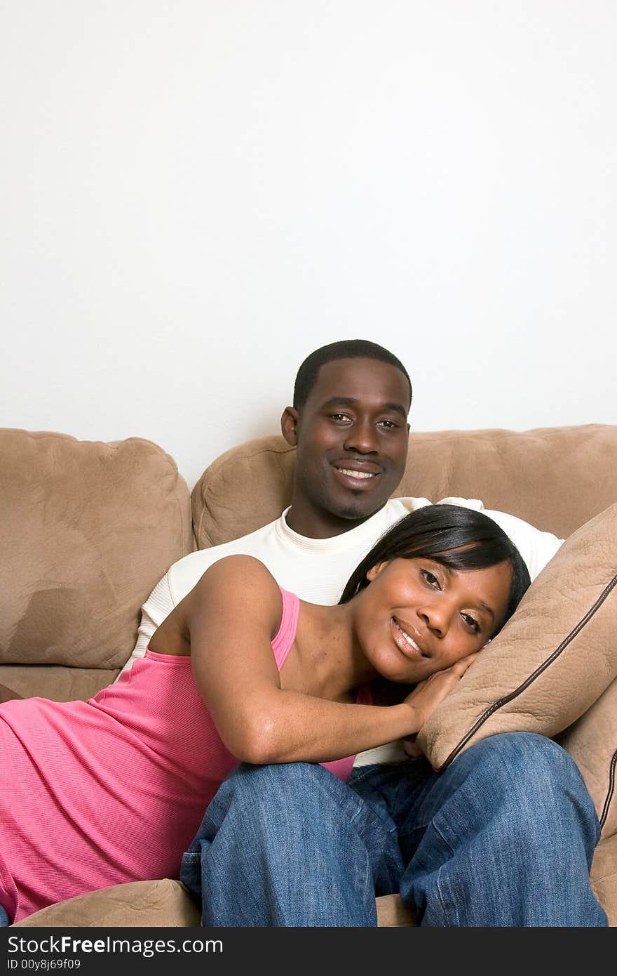 Attractive smiling young couple relaxing on a sofa.  The man is sitting, and the woman lying with her head in his lap.  Vertically  framed shot with copy-space above the sofa. Attractive smiling young couple relaxing on a sofa.  The man is sitting, and the woman lying with her head in his lap.  Vertically  framed shot with copy-space above the sofa.