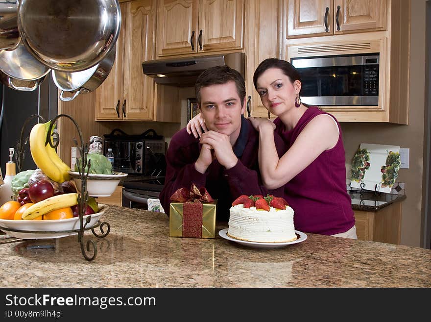 Attractive couple leaning on their kitchen counter which is covered with a cake and a present. They have a neutral expression on their faces and are looking at the camera. Horizontally framed shot. Attractive couple leaning on their kitchen counter which is covered with a cake and a present. They have a neutral expression on their faces and are looking at the camera. Horizontally framed shot.