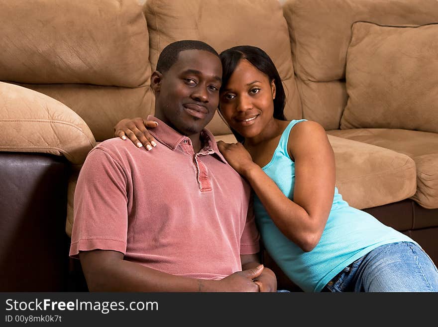 A young couple sitting together on the floor by a sofa. Horizontally framed shot. A young couple sitting together on the floor by a sofa. Horizontally framed shot.