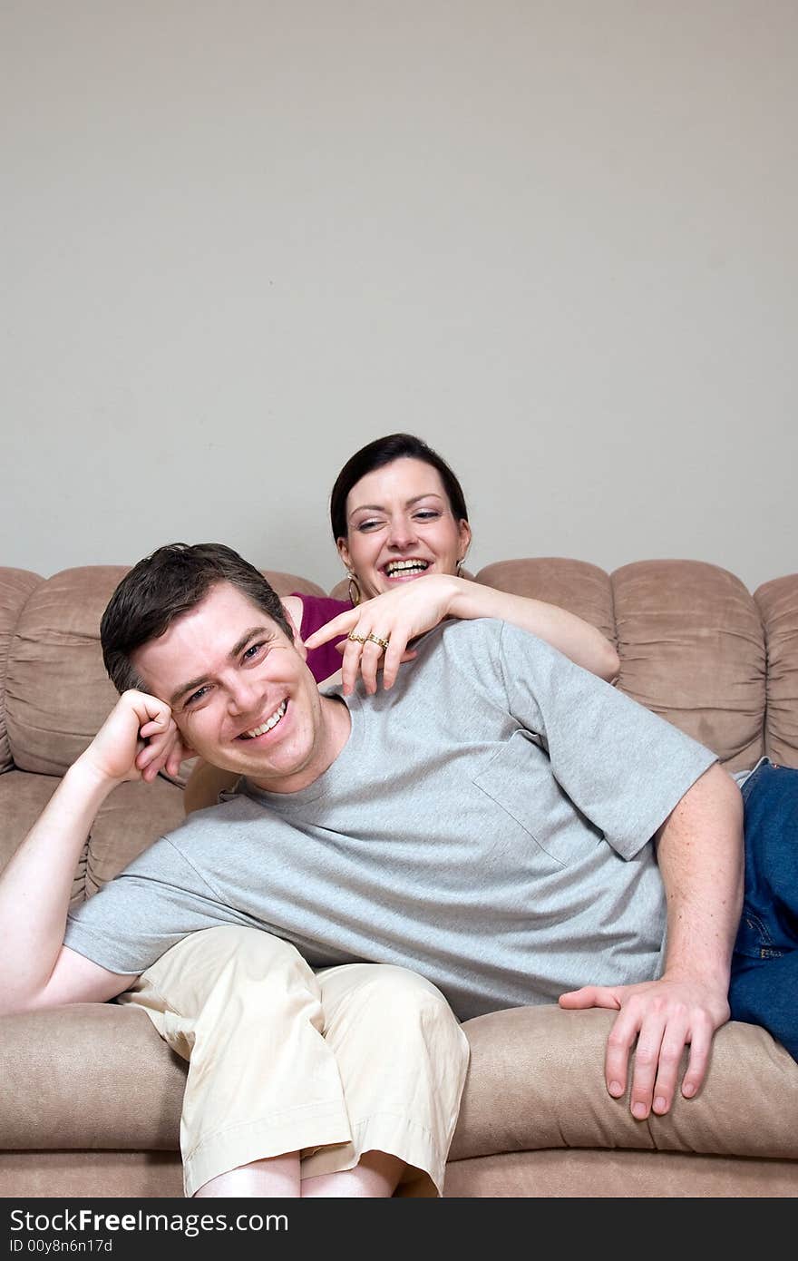 Couple horsing around on their living room couch. He is lying in her lap and she is tickling his ear. Both are laughing at the camera. Vertically framed shot. Couple horsing around on their living room couch. He is lying in her lap and she is tickling his ear. Both are laughing at the camera. Vertically framed shot.