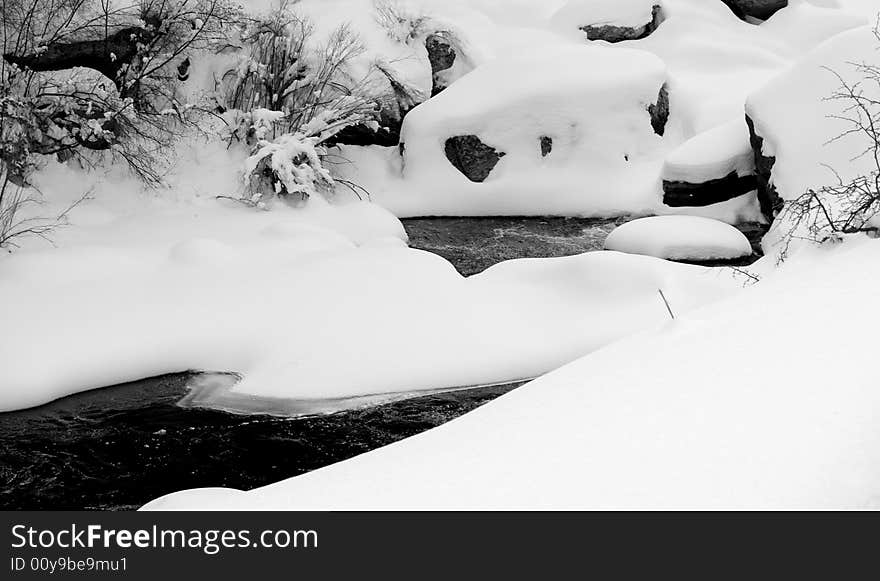 Snow drifts create unusual shapes over the boulders of a mountain river in Colorado. Snow drifts create unusual shapes over the boulders of a mountain river in Colorado.