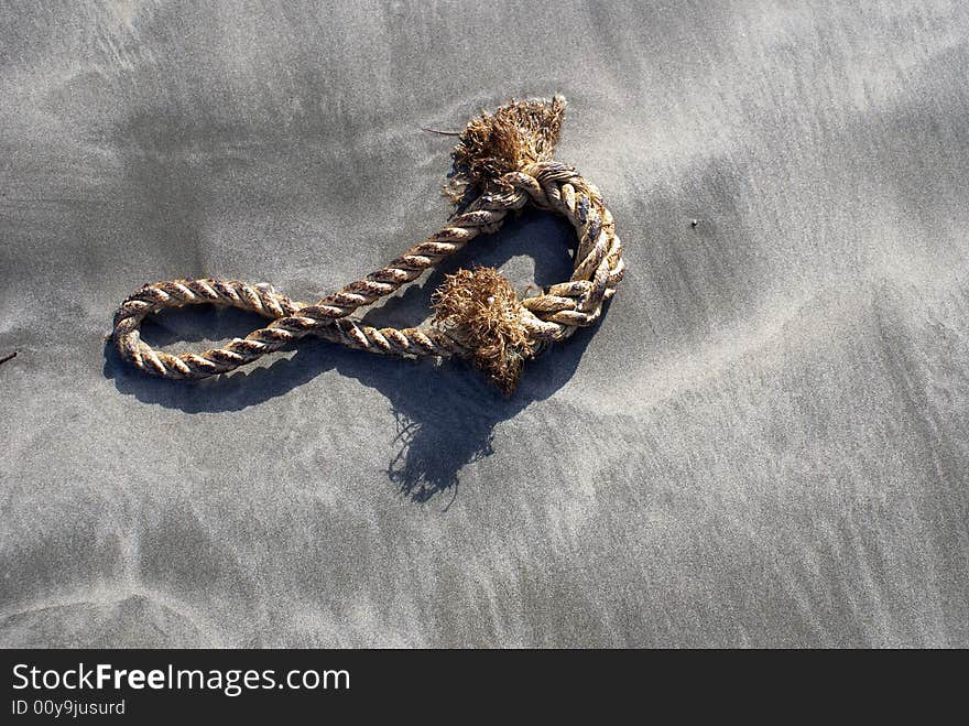 A old brown rope staying on the grain beach with sand.