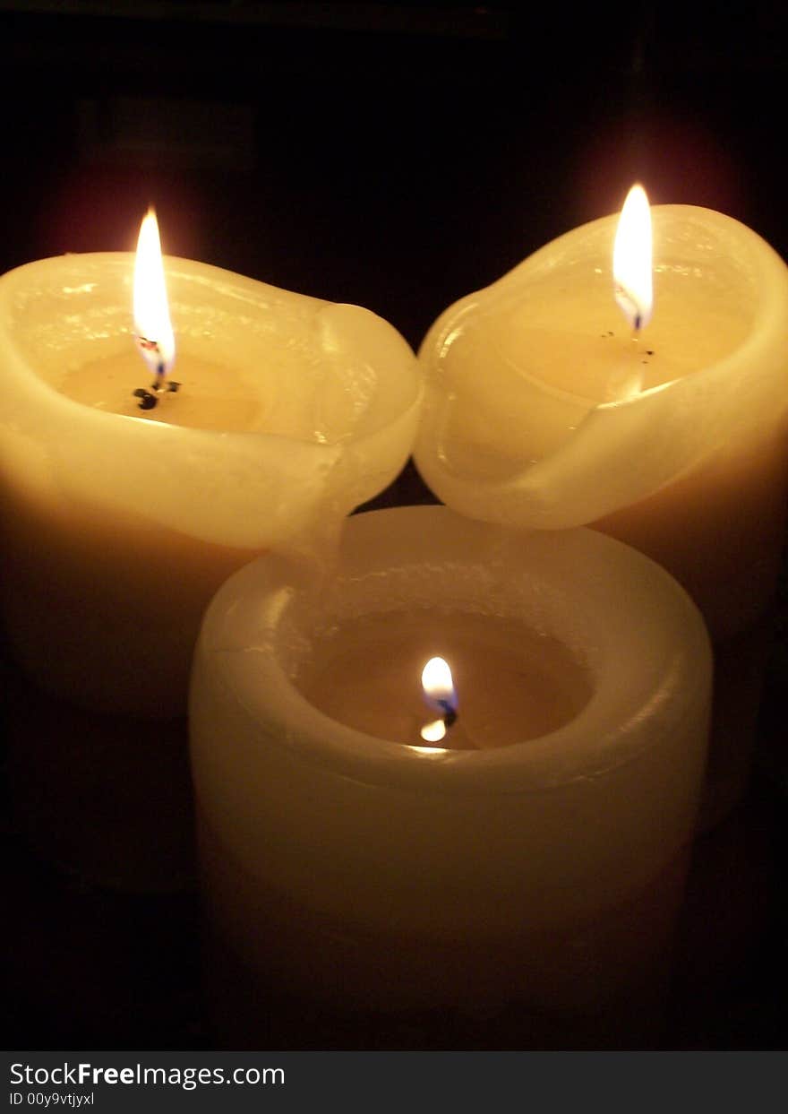 Three burning candles. Two taller melting into the shorter. Three burning candles. Two taller melting into the shorter.