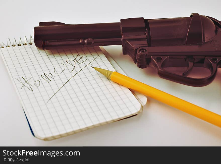 Close-up of a notepad with word 'homicide' written with pencil and gun with selective focus