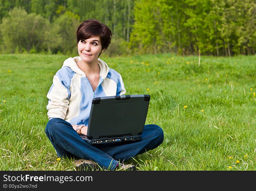 Young attractive girl sits on a green grass with a portable computer. Young attractive girl sits on a green grass with a portable computer