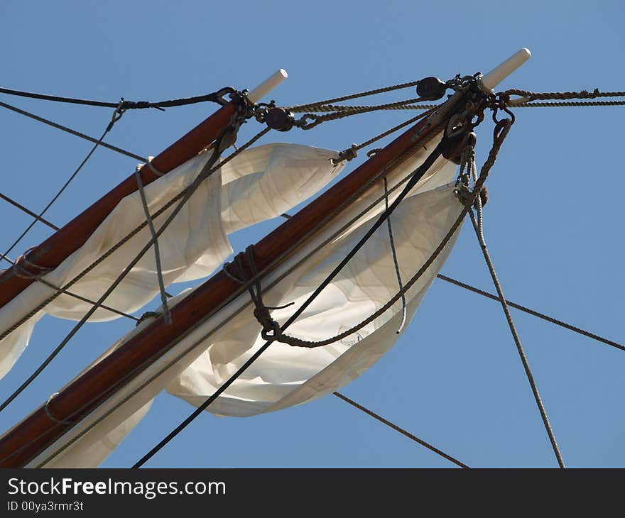 2 yards with sails partly unwounded of a sailing boat against a blue sky. 2 yards with sails partly unwounded of a sailing boat against a blue sky