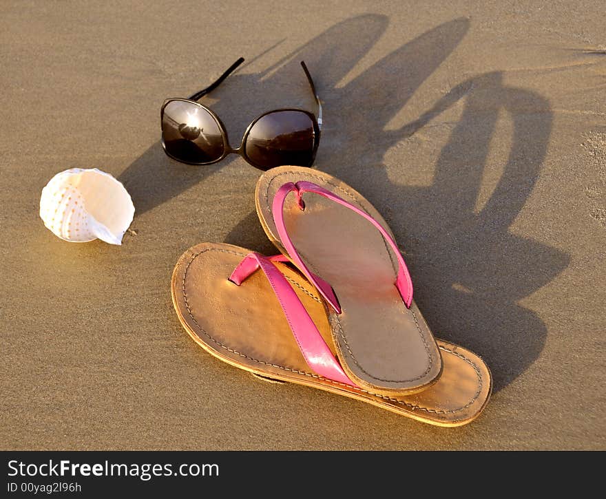 Close up of slippers, sunglasses and shell on sand background. Close up of slippers, sunglasses and shell on sand background