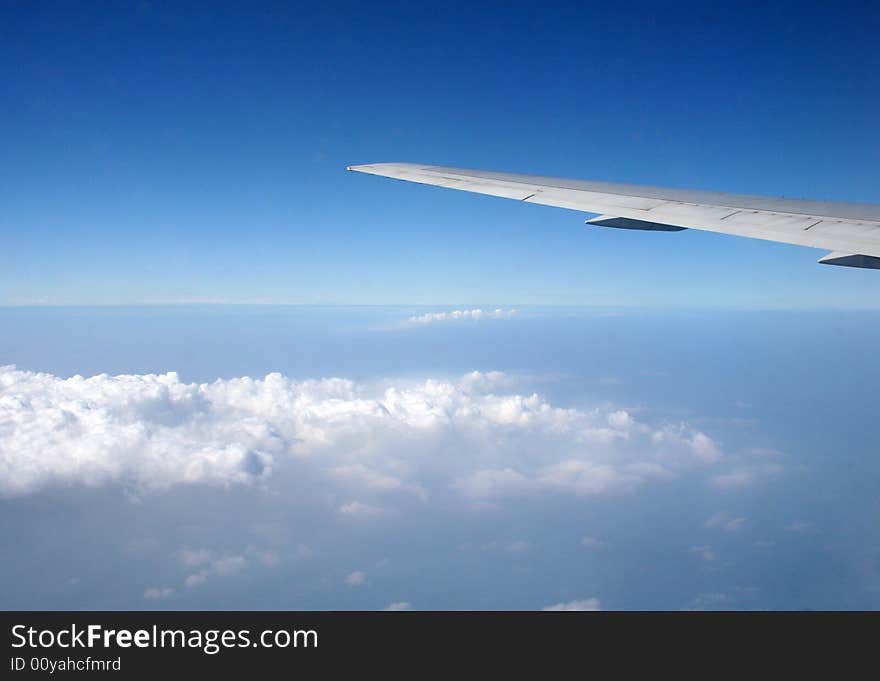 An airplane wing is seen from the window of a jet and is overlooking the clouds.