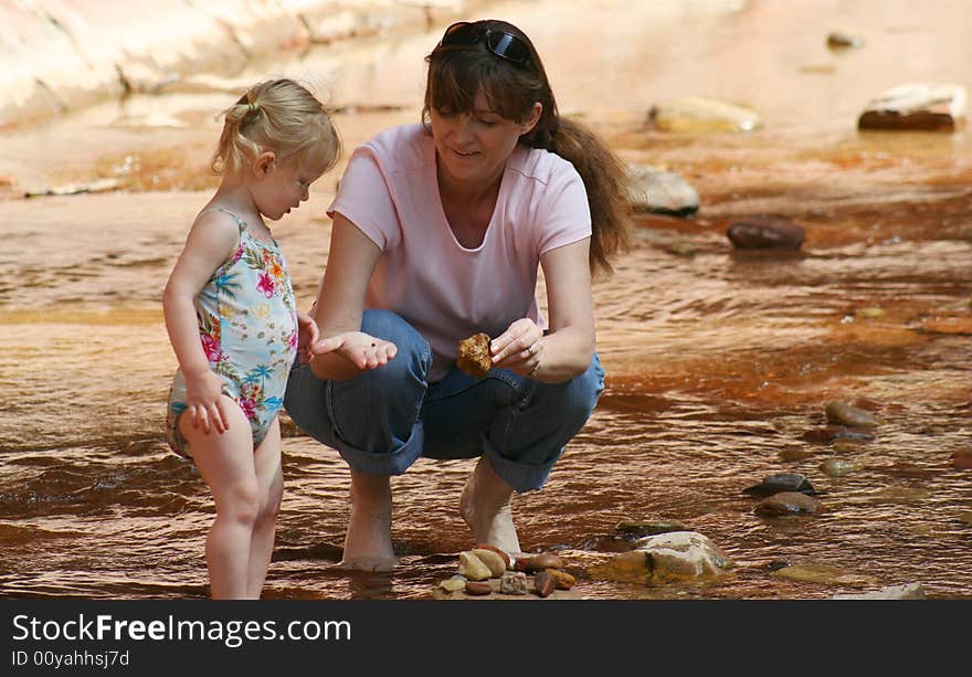 A Woman Shows a Toddler an Interesting Rock While Wading in a Shallow Creek. A Woman Shows a Toddler an Interesting Rock While Wading in a Shallow Creek