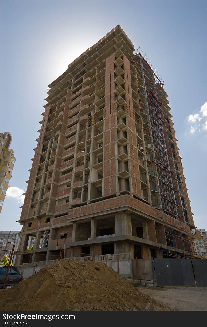 A towering building under construction against blue sky; the sun is behind the building