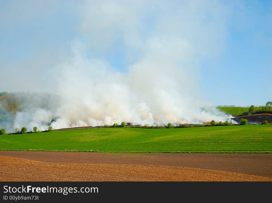 Field on fire with green pasture and blue sky. Field on fire with green pasture and blue sky